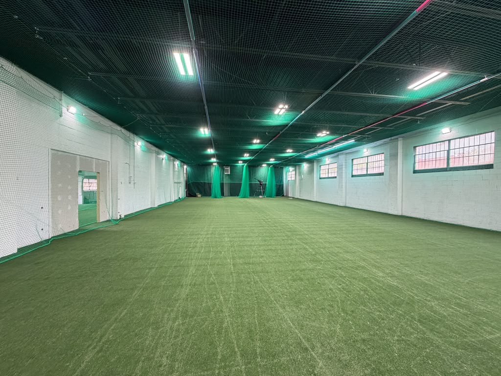 Wide view of the Bat n Ball indoor turf floor with retractable lane nets and bowling machines at the far end