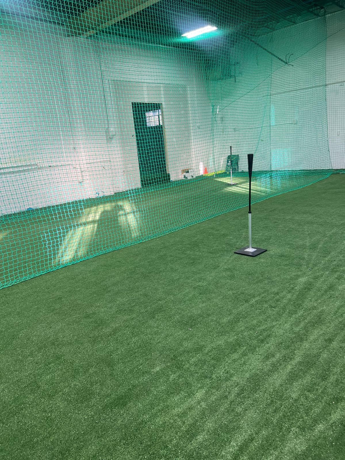 Batting tee on green turf inside a netted practice lane